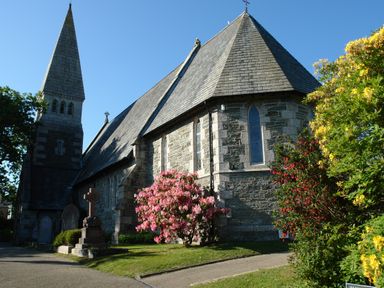 A stone church building with a tall steeple surrounded by flowering bushes at Regatta Cottage in Feock