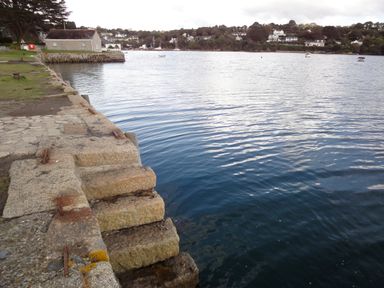 A waterfront with stone steps leading into the water and houses visible across the river at Regatta Cottage in Feock