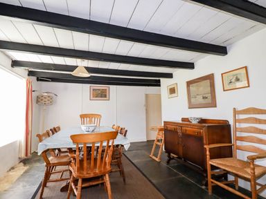 A dining room with a wooden table and chairs a sideboard with framed pictures on the wall at Polcreek Farmhouse in Veryan