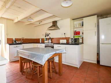 A kitchen with a wooden table and stools a dishwasher stove and refrigerator at Polcreek Farmhouse in Veryan