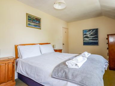 A bedroom with a double bed white pillows white towels on a blanket two paintings on the walls at Polcreek Farmhouse in Veryan