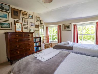 A bedroom with two single beds a wooden dresser a bookshelf and framed pictures on the wall at Polcreek Farmhouse in Veryan