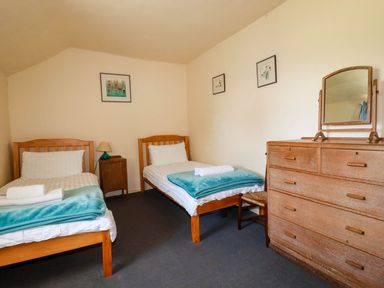 A bedroom with two single beds a wooden dresser with a mirror and framed pictures on the wall at Polcreek Farmhouse in Veryan