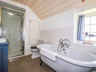 A bathroom with a bathtub a toilet a shower and a window with a bird figurine at Polcreek Farmhouse in Veryan