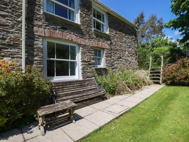 A stone house exterior with windows a wooden bench a small wooden table and garden steps at Polcreek Farmhouse in Veryan