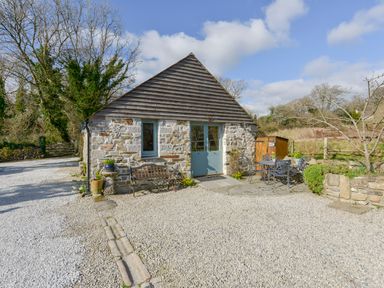 A small stone and wood cottage with a bench and an outdoor table with chairs at Hideaway Barn in Charlestown