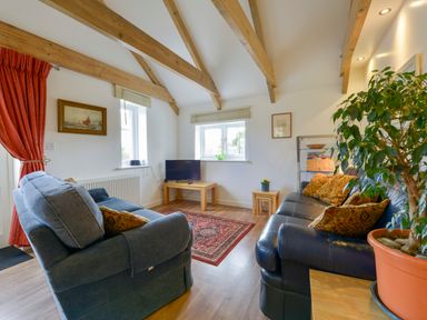 A living room with exposed wooden beams two sofas a small TV on a wooden table and a potted plant at Hideaway Barn in Charlestown
