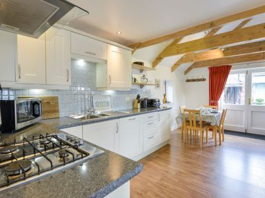 A kitchen with white cabinets a gas stove a sink and a dining table with chairs at Hideaway Barn in Charlestown