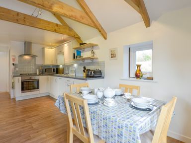 A kitchen with wooden beams a dining table set with tea cups and a window with a vase at Hideaway Barn in Charlestown