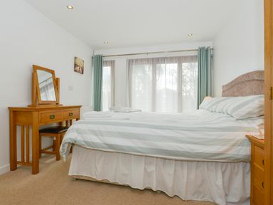 A bedroom with a bed striped bedding wooden dressing table and windows with curtains at Hideaway Barn in Charlestown
