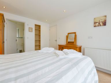A bedroom with a bed striped bedspread towels on the bed a wooden dresser with a mirror a wooden wardrobe an open door to a bathroom and a wall radiator at Hideaway Barn in Charlestown