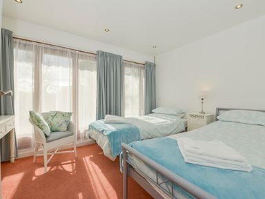 A bedroom with two single beds a chair with cushions a bedside table and large windows with curtains at Hideaway Barn in Charlestown