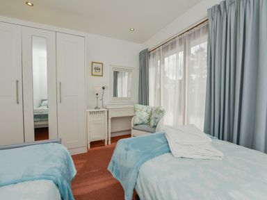 A bedroom with two single beds a wardrobe a dressing table a chair with cushions and curtains at Hideaway Barn in Charlestown