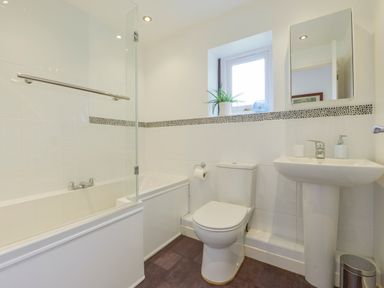 A bathroom with a bathtub shower with glass screen a toilet a pedestal sink and a small window with a plant at Hideaway Barn in Charlestown