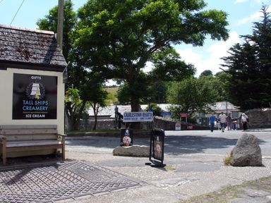 A street scene with a bench and tall ships creamery sign near trees and people walking at Hideaway Barn in Charlestown