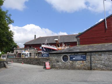 Exterior view of a shipwreck and heritage centre with a rescue boat on display and signage at Hideaway Barn in Charlestown