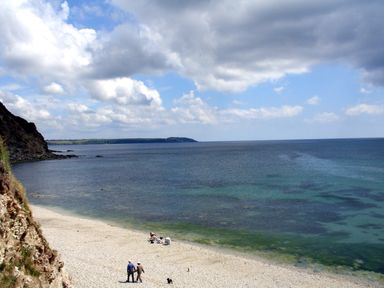 A rocky beach with people walking and sitting near the water under a partly cloudy sky at Hideaway Barn in Charlestown