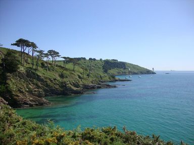 A coastal landscape with trees on cliffs and boats in the water at Stones Throw in St Mawes