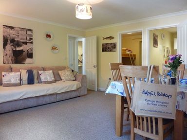 A living room with a sofa and cushions next to a dining table with chairs and flowers at Stones Throw in St Mawes