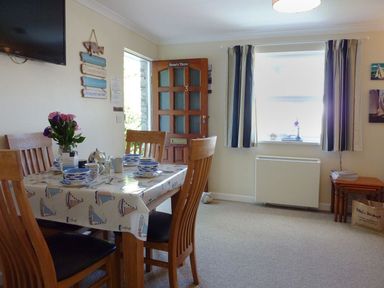 A dining area with a wooden table set for four next to a window and an open door at Stones Throw in St Mawes