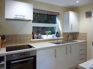 A kitchen counter with a stove oven sink cabinets and a window with flowers on the sill at Stones Throw in St Mawes