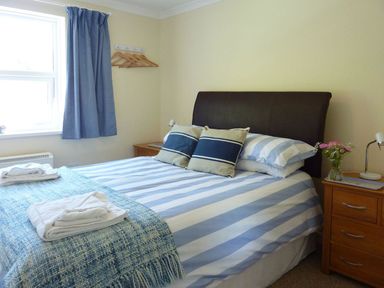 A bedroom with a bed with blue and white striped bedding and two blue cushions at Stones Throw in St Mawes
