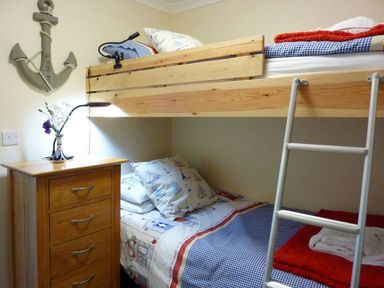 A bedroom with a wooden bunk bed a wooden chest of drawers with a lamp and flowers and a wall decoration shaped like an anchor at Stones Throw in St Mawes