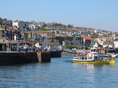 A harbor with a yellow ferry boat approaching the dock and houses on a hillside in the background at Primrose Cottage in Penryn