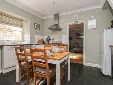 A kitchen with a wooden table set for four with chairs a stove and a refrigerator with a view into an adjoining room at Primrose Cottage in Penryn