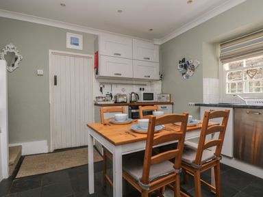 A kitchen with a wooden dining table set for four near a window and cabinets at Primrose Cottage in Penryn
