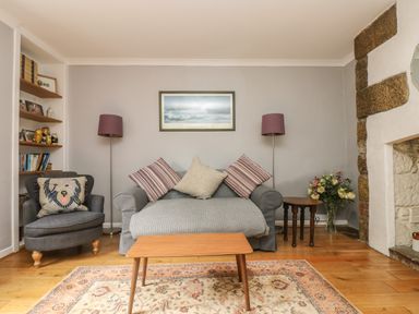 A living room with a sofa and armchair with cushions a coffee table and a fireplace at Primrose Cottage in Penryn
