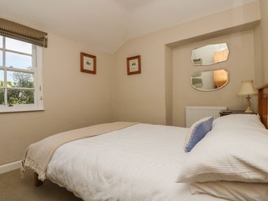A bedroom with a double bed bedside table lamp two mirrors and framed pictures at Primrose Cottage Penryn