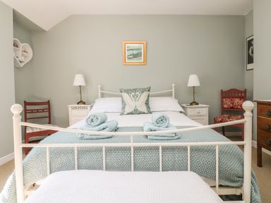 A bedroom with a white metal bed frame folded towels bedside tables floor lamps and chairs at Primrose Cottage Penryn