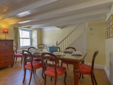 A dining room with a wooden table set for six and chairs with red cushions at April Cottage in Coverack