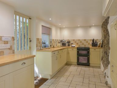 A kitchen with cream cabinets a black oven a microwave and a wooden countertop at April Cottage in Coverack