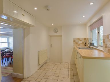 A kitchen with tiled floor a sink and cabinets a door and a wall clock at April Cottage in Coverack