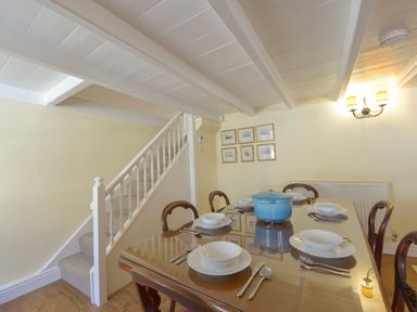 A dining room with a table set for six and a staircase in the background at April Cottage in Coverack