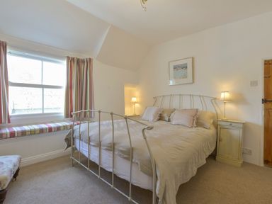 A bedroom with a metal bed frame two bedside tables with lamps a window with striped curtains and a window seat at April Cottage in Coverack