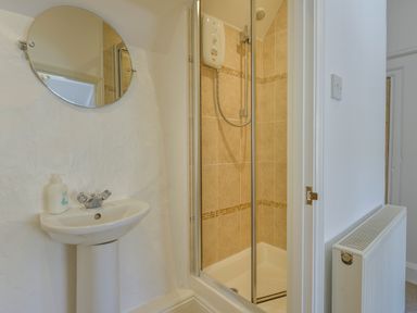 A bathroom with a sink a round mirror a shower cubicle and a radiator at April Cottage in Coverack