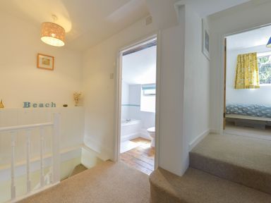 A hallway with stairs leading down and two doorways showing a bathroom and a bedroom at April Cottage in Coverack