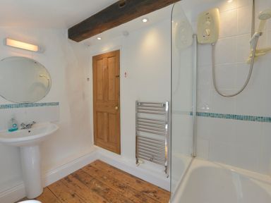 A bathroom with a sink mirror wooden door towel radiator and shower at April Cottage in Coverack