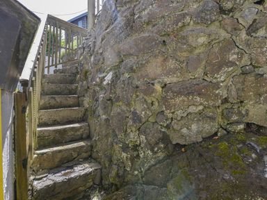 Stone steps with wooden railing next to a stone wall outdoors at April Cottage in Coverack
