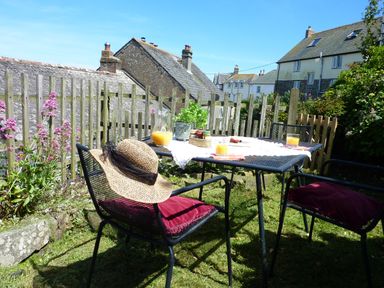 An outdoor garden area with a metal table and chairs with cushions and a straw hat at April Cottage in Coverack