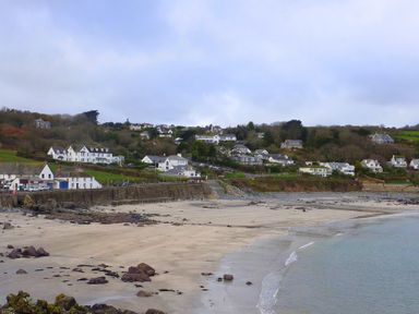 A sandy beach with rocks and houses on a hillside in the background at April Cottage in Coverack