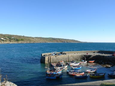 A small harbor with boats moored inside next to a stone pier and a coastline in the background at April Cottage in Coverack