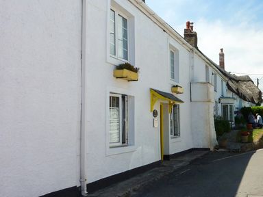 A row of white houses with flower boxes and a yellow door frame along a street at April Cottage in Coverack