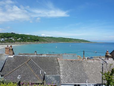 A coastal view with rooftops in the foreground and boats on water at April Cottage in Coverack