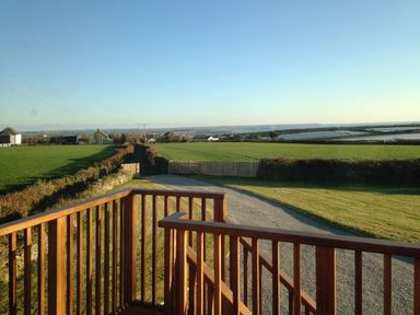 A view over a gravel driveway and green fields from a wooden balcony railing at The Hayloft in Breage