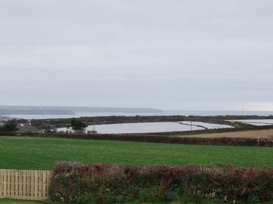 A landscape with green fields hedges and a wooden fence with water and hills in the background at The Hayloft in Breage