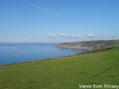 A grassy coastal cliff overlooking a calm sea with a headland in the distance at The Hayloft in Breage